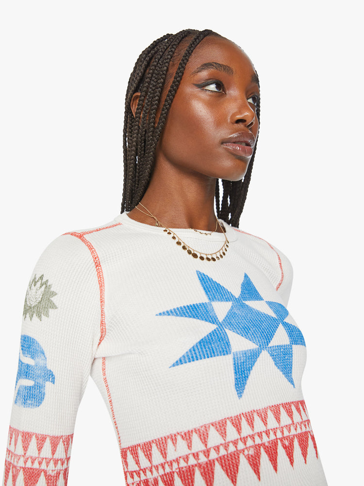 Close up view of a woman shrunken long sleeve thermal with a crewneck and slightly curved hem in an off white with faded star symbols on chest and arms.