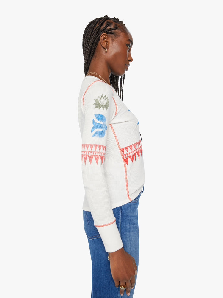 Side view of a woman shrunken long sleeve thermal with a crewneck and slightly curved hem in an off white with faded star symbols on chest and arms.