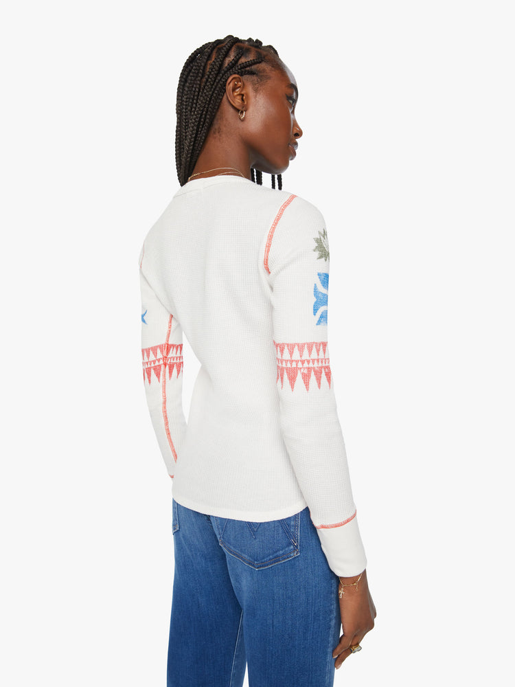Back view of a woman shrunken long sleeve thermal with a crewneck and slightly curved hem in an off white with faded star symbols on chest and arms.