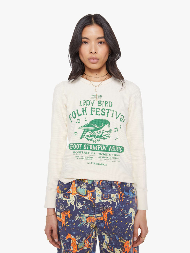 Front view of a woman in a an off-white with a green music festival-inspired graphic on the front and text in orange on the back thermal tee.