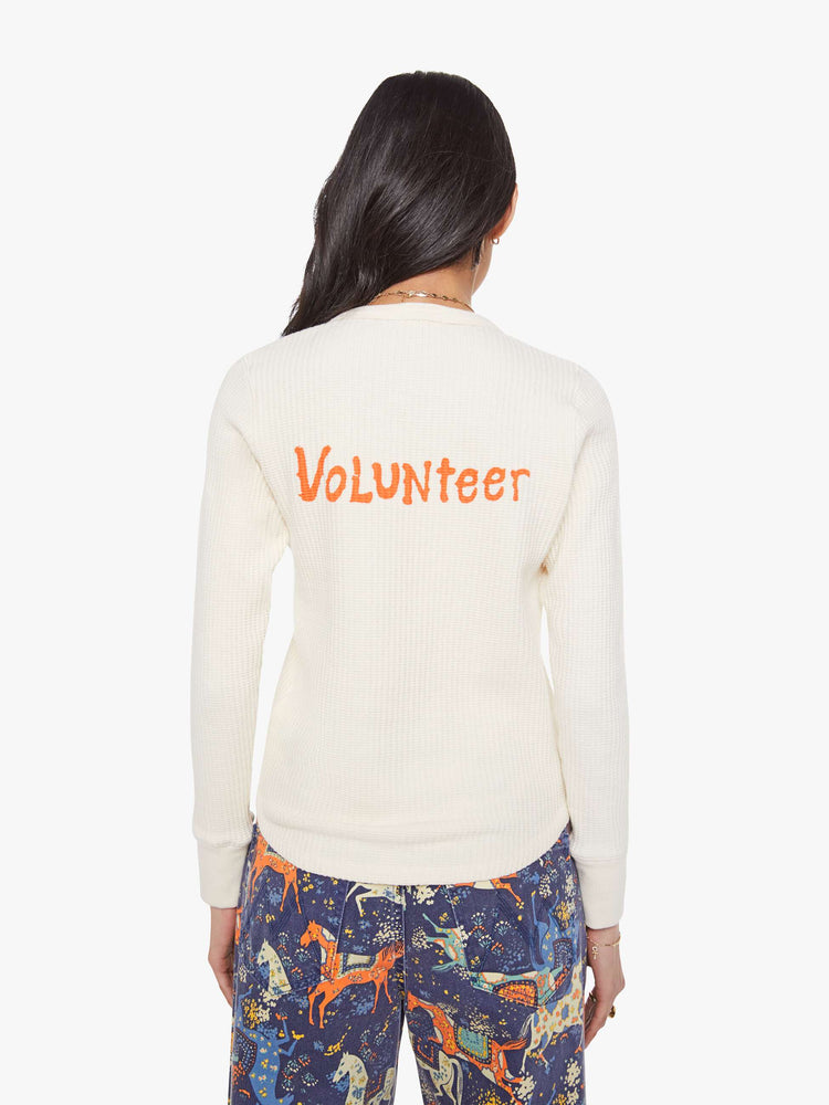 Back view of a woman in a an off-white with a green music festival-inspired graphic on the front and text in orange on the back thermal tee.