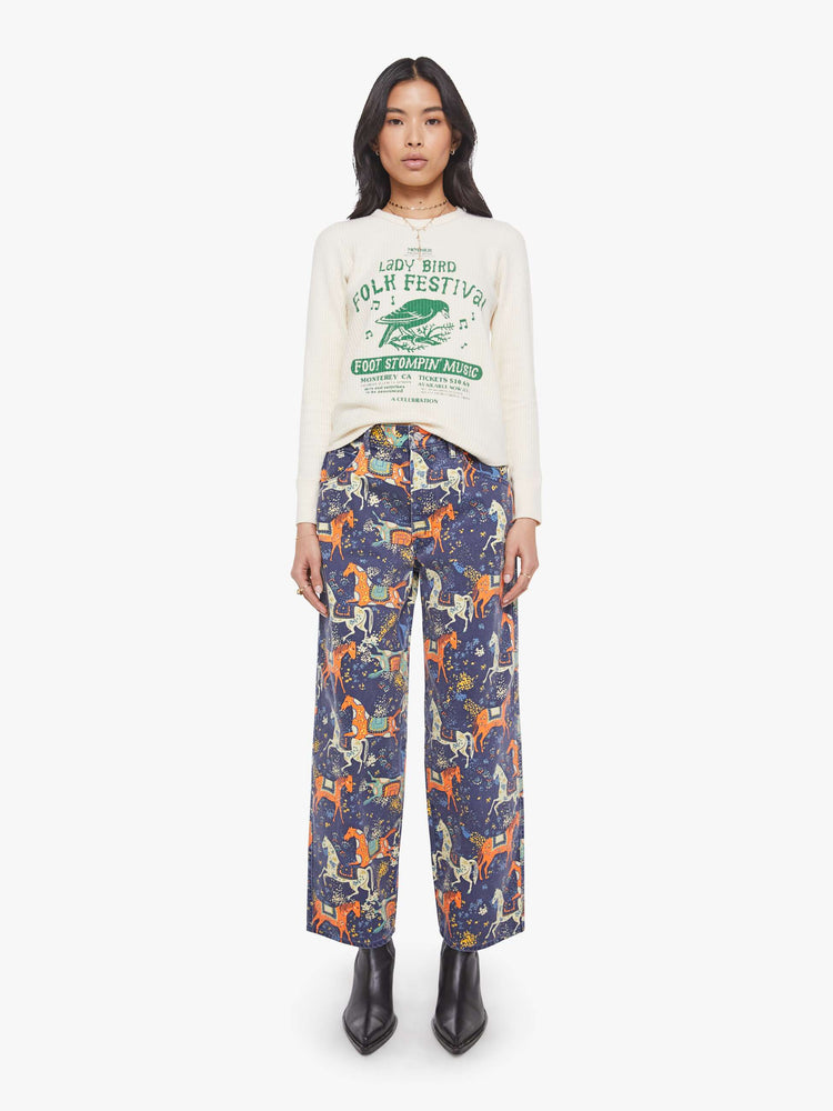 Full body view of a woman in a an off-white with a green music festival-inspired graphic on the front and text in orange on the back thermal tee.