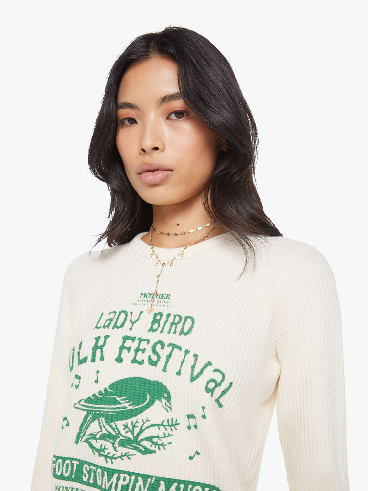 Close up view of a woman in a an off-white with a green music festival-inspired graphic on the front and text in orange on the back thermal tee.