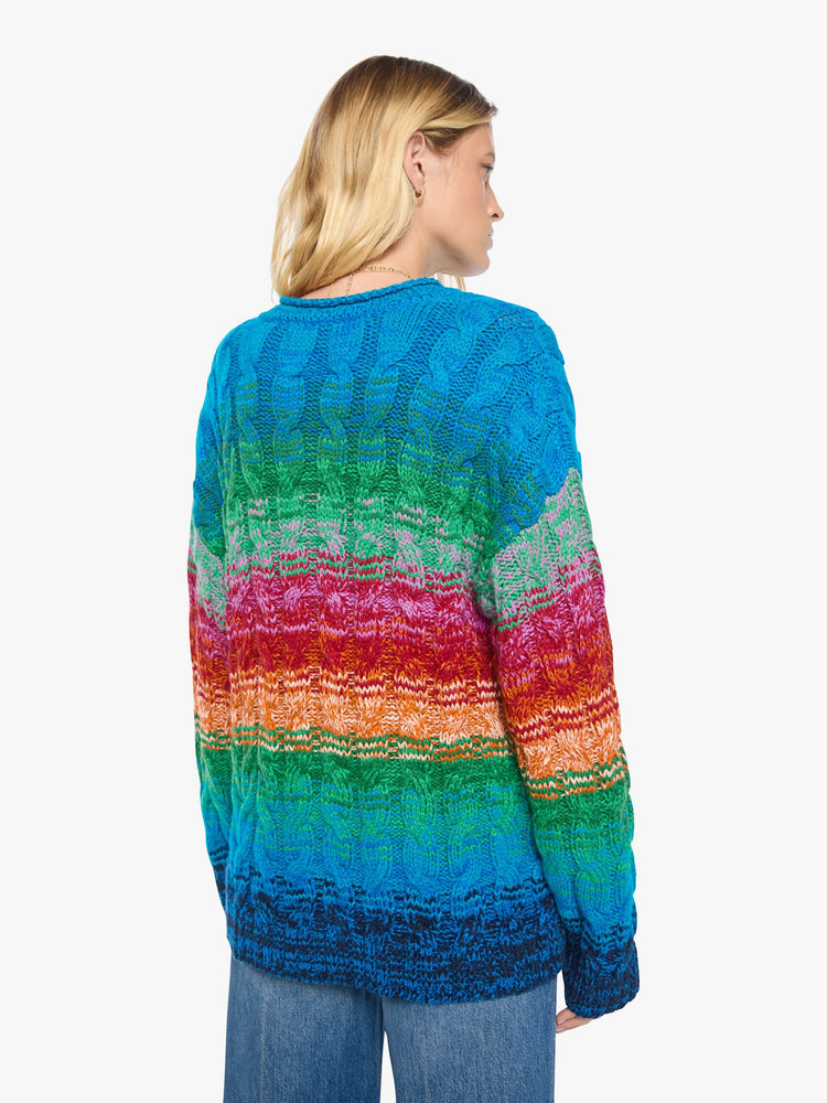 Back view of a woman in a cardigan is designed in a rainbow stripe pattern with cable knit details.