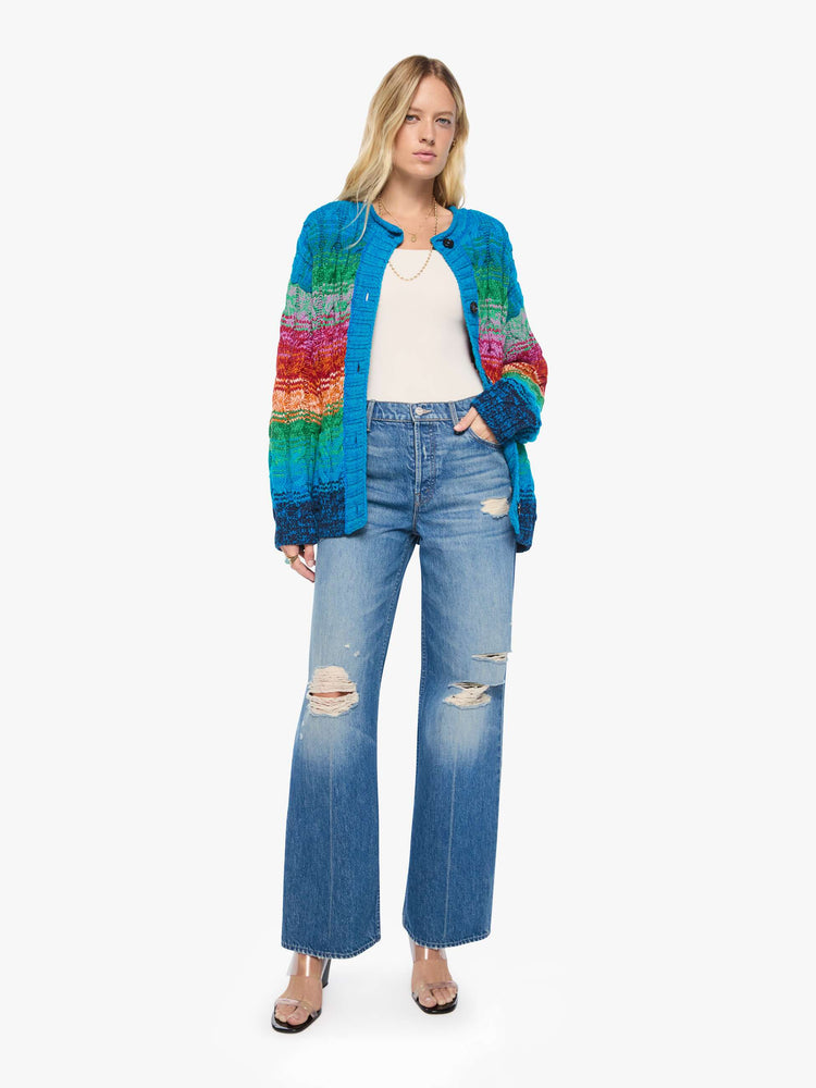 Full body view of a woman in a cardigan is designed in a rainbow stripe pattern with cable knit details.
