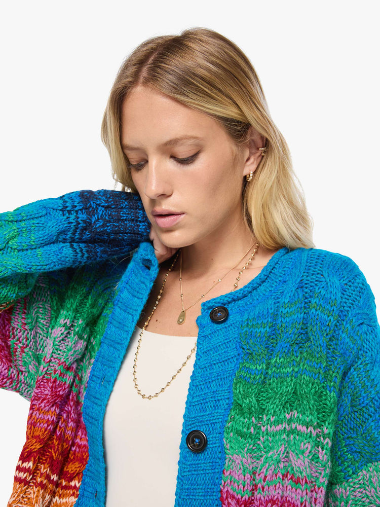 Close up view of a woman in a cardigan is designed in a rainbow stripe pattern with cable knit details.