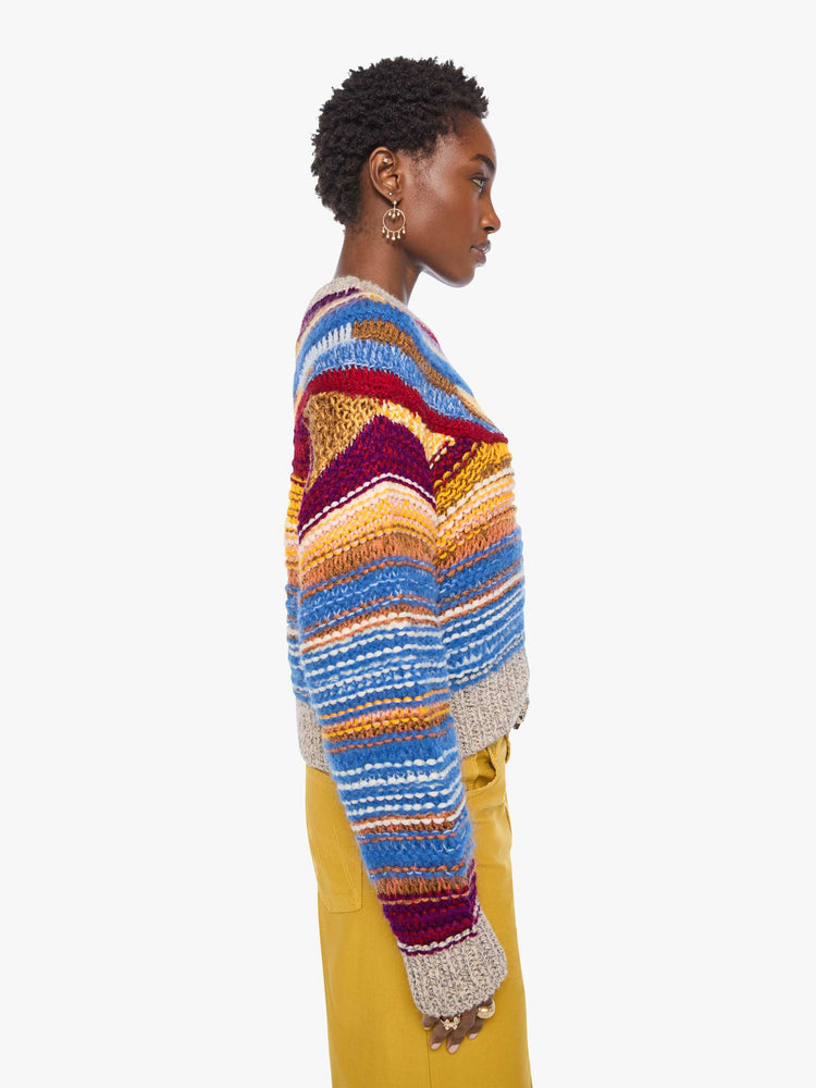 Side view of a woman in a crewneck sweater is designed with colorful horizontal stripes, textured details and ribbed grey hems.