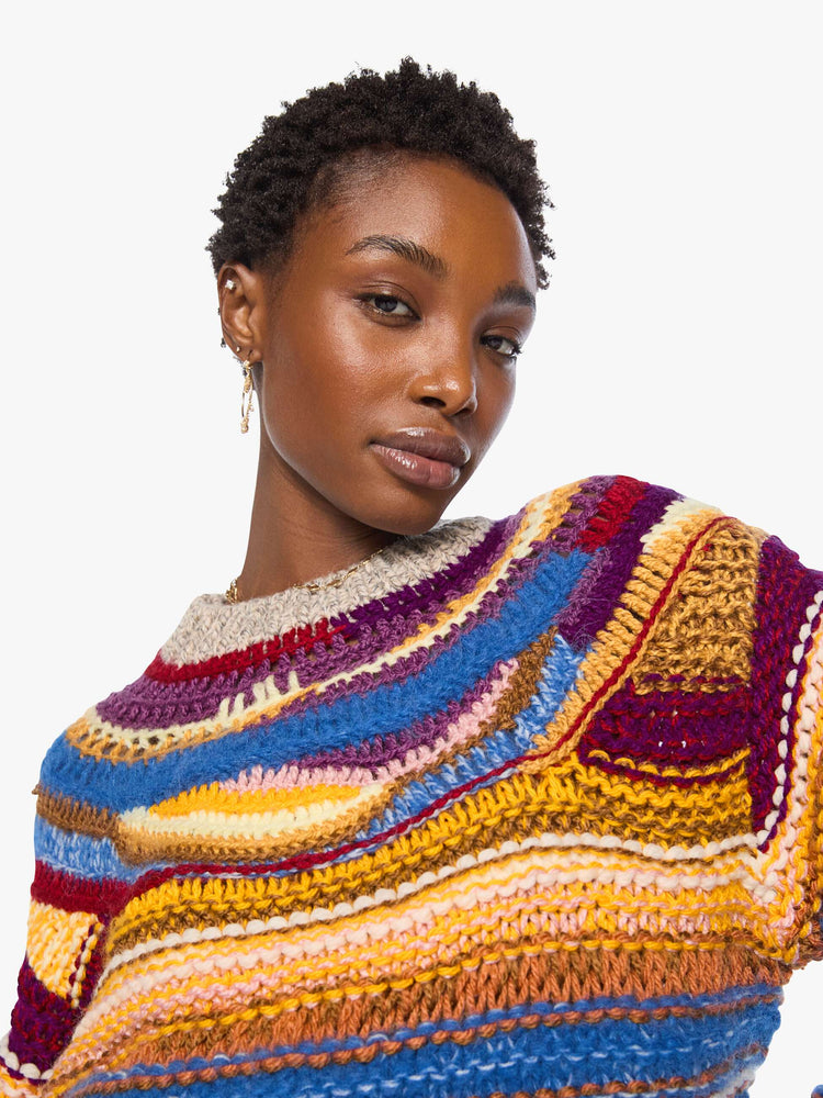 Close up view of a woman in a crewneck sweater is designed with colorful horizontal stripes, textured details and ribbed grey hems.
