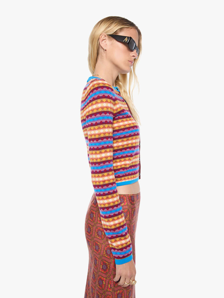Side view of a woman in a golden yellow, maroon, white and blue jacquard-print stripes shrunken crewneck cardigan with snap closures down the front.