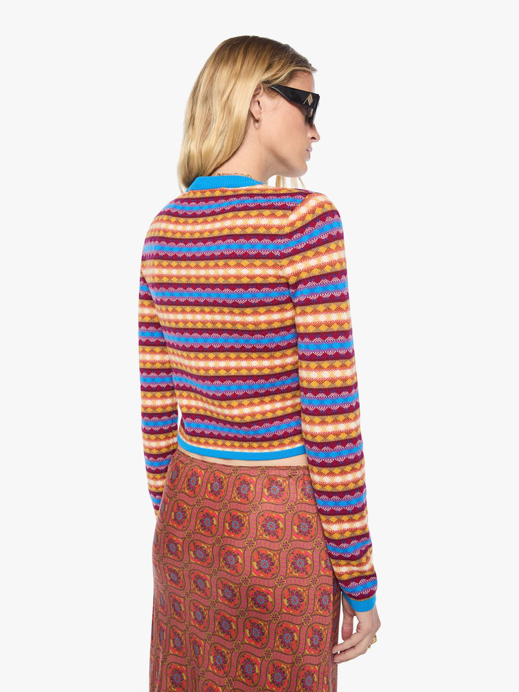 Back view of a woman in a golden yellow, maroon, white and blue jacquard-print stripes shrunken crewneck cardigan with snap closures down the front.