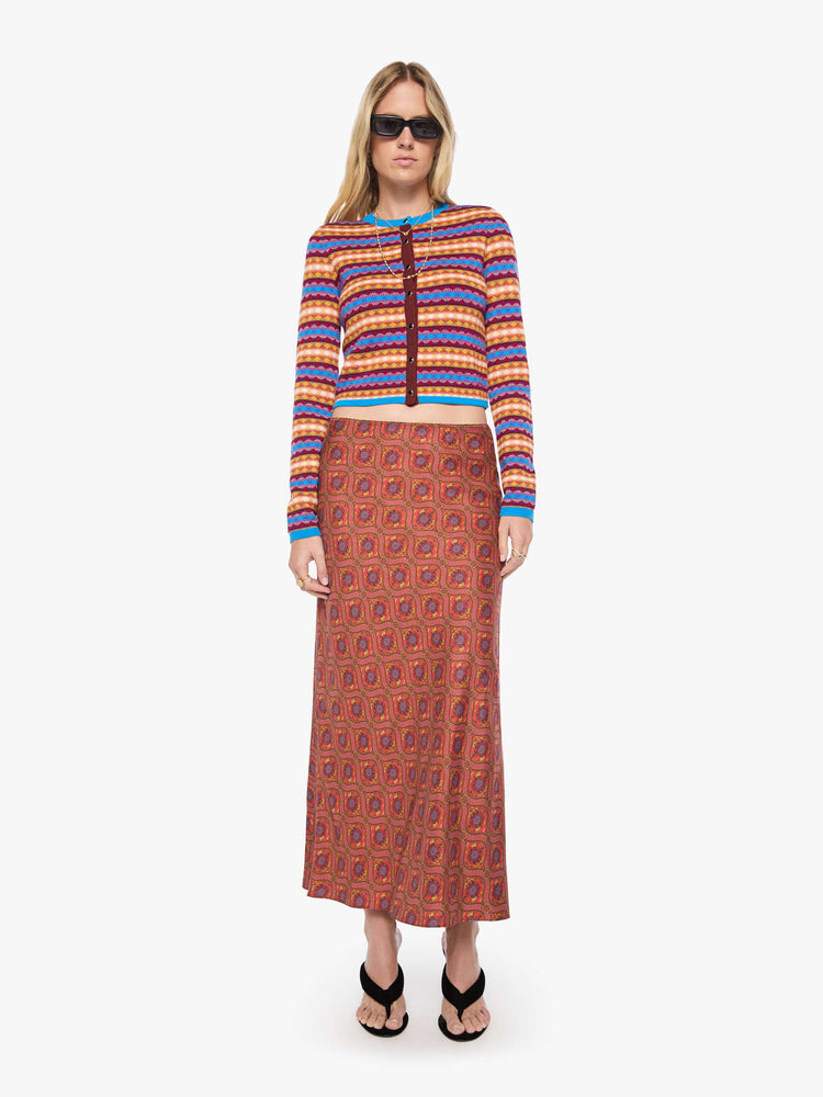 Full body view of a woman in a golden yellow, maroon, white and blue jacquard-print stripes shrunken crewneck cardigan with snap closures down the front.