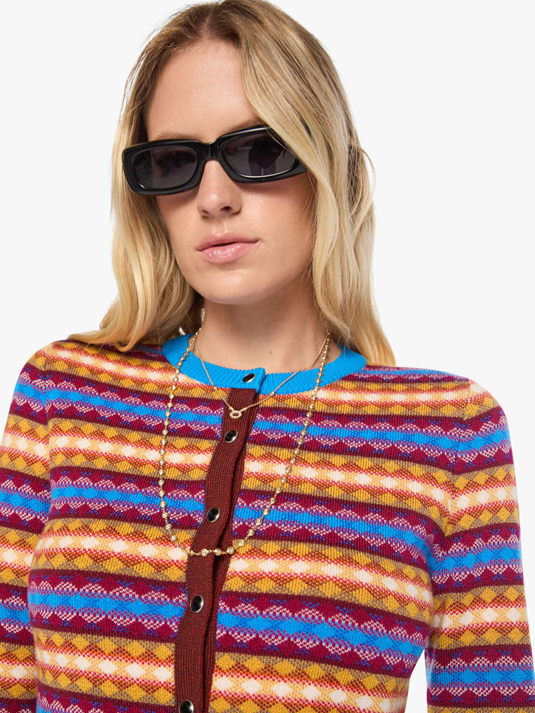 Close up view of a woman in a golden yellow, maroon, white and blue jacquard-print stripes shrunken crewneck cardigan with snap closures down the front.
