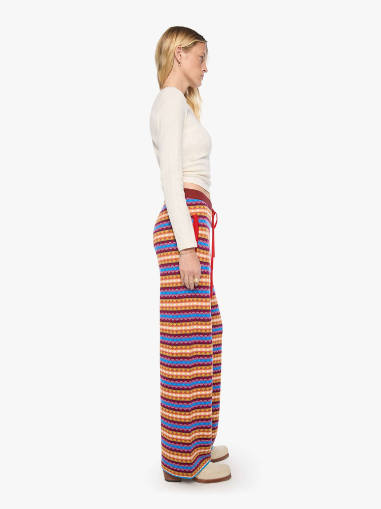 Side view of a woman in a golden yellow, maroon, white and blue jacquard-print stripes wide-leg pants with an elastic drawstring waistband and a loose, comfortable fit.