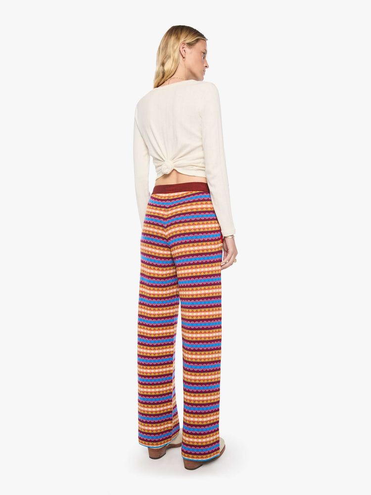 Back view of a woman in a golden yellow, maroon, white and blue jacquard-print stripes wide-leg pants with an elastic drawstring waistband and a loose, comfortable fit.