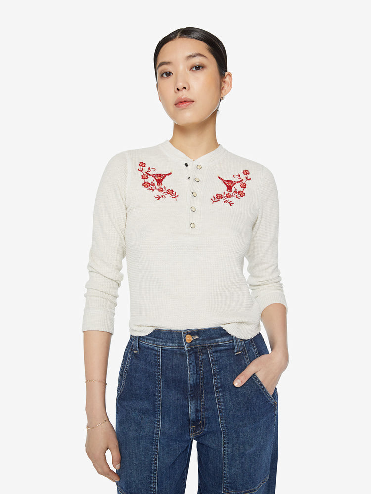 Front view of a woman shrunken long sleeve henley with a buttoned crewneck and a cropped hem in a creamy off white with red embroidery on the front.