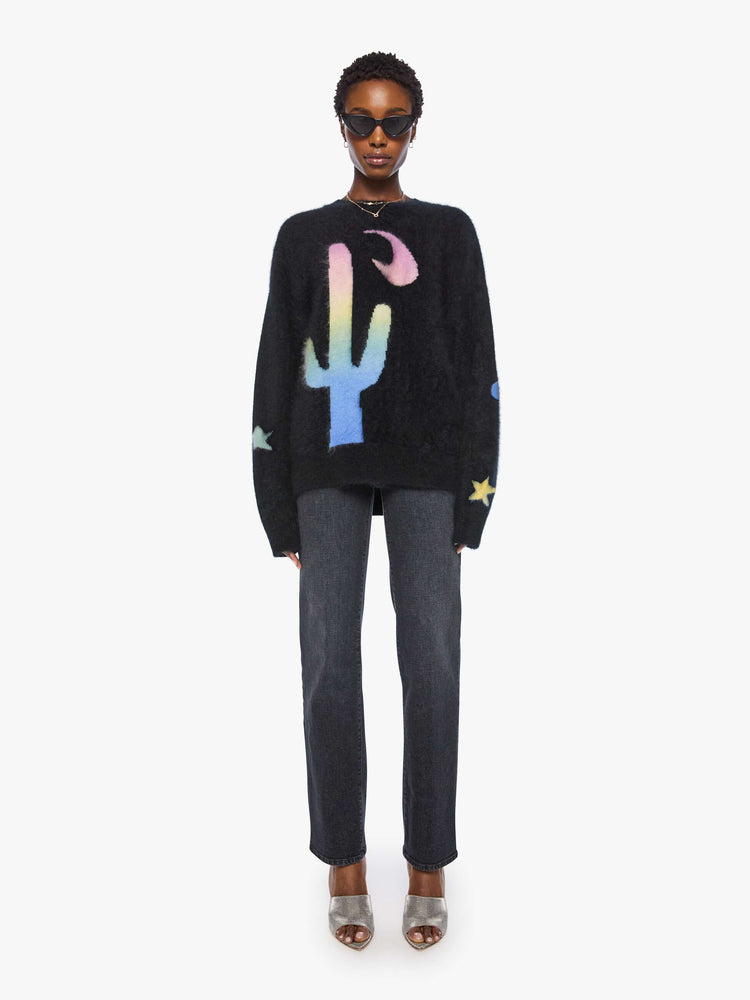 Full body view of a woman in sweater is designed in black with a rainbow cactus and moon across the chest.