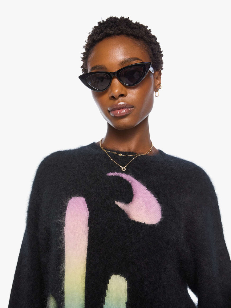 Close up view of a woman in sweater is designed in black with a rainbow cactus and moon across the chest.