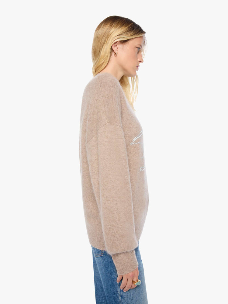 Side view of a woman in a sweater designed in a warm tan with a knit Pegasus graphic in light blue on the front and MOTHER's name on the hip.
