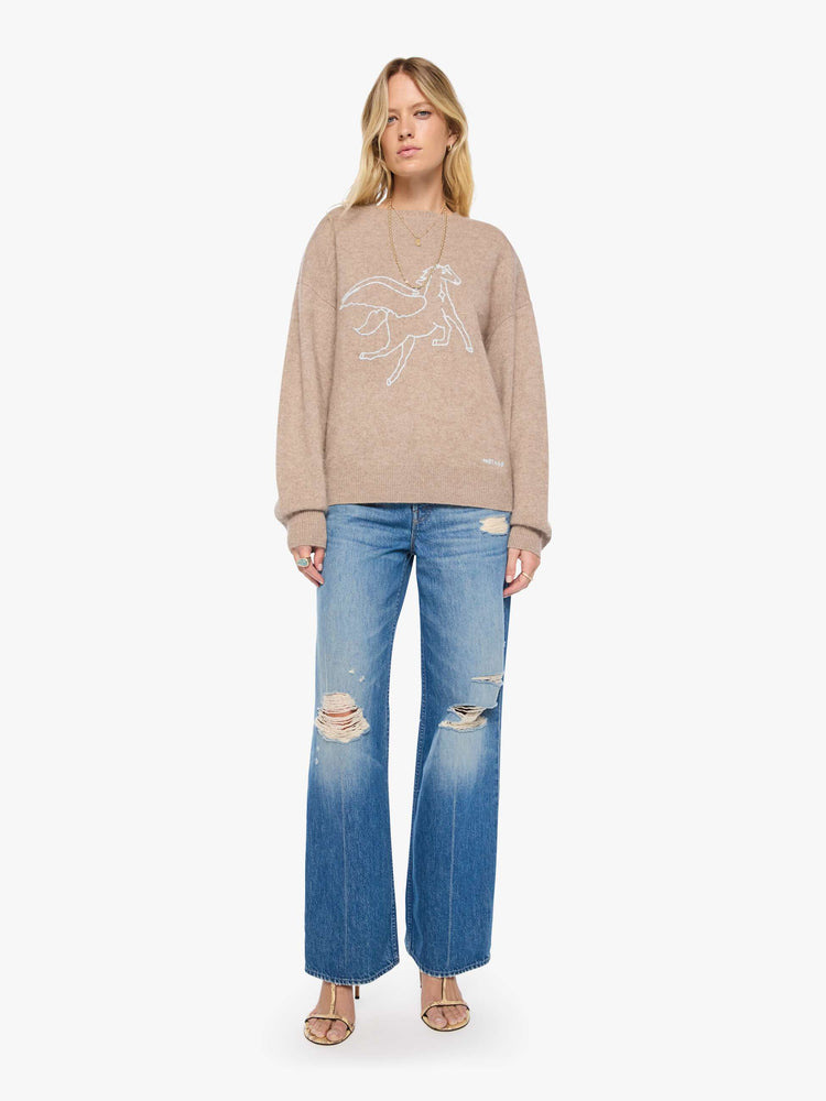 Full body view of a woman in a sweater designed in a warm tan with a knit Pegasus graphic in light blue on the front and MOTHER's name on the hip.