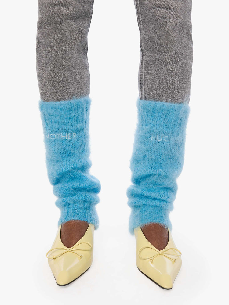 Front view of a woman in a legwarmer designed in a  bright light blue mohair blend with ribbed hems and MOTHER FUCKER in white across the front.