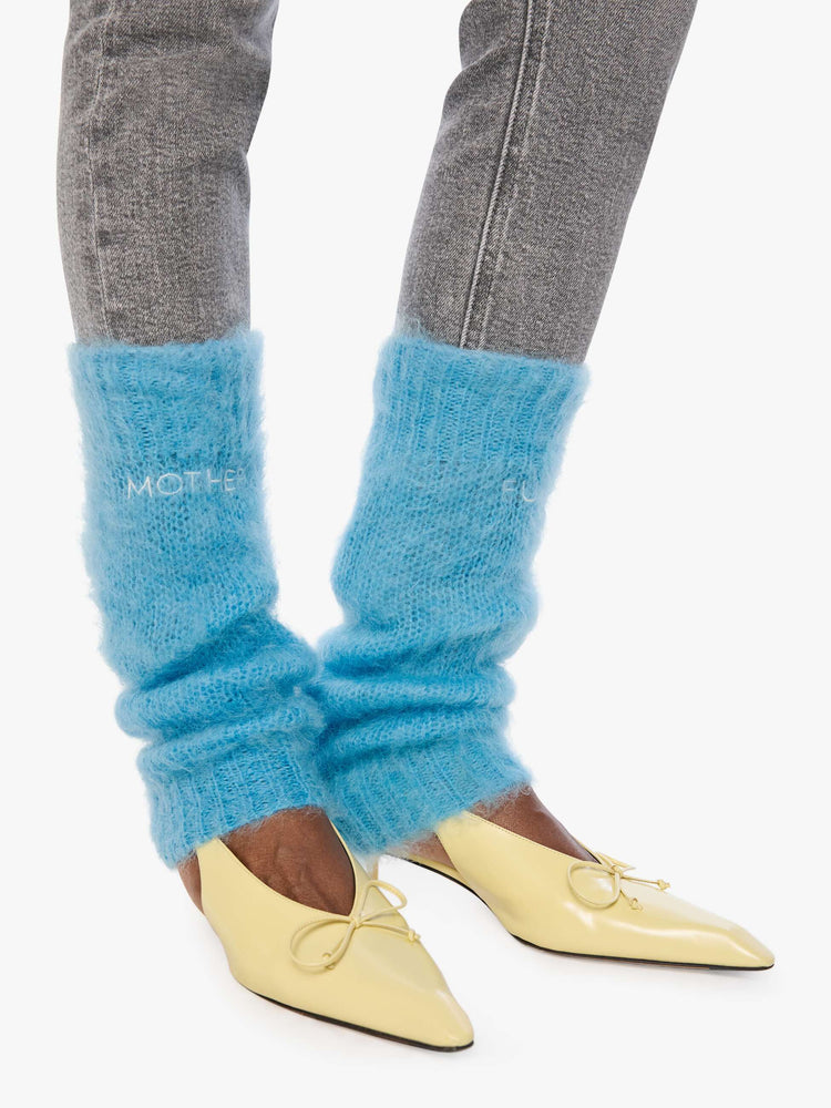 Side view of a woman in a legwarmer designed in a  bright light blue mohair blend with ribbed hems and MOTHER FUCKER in white across the front.