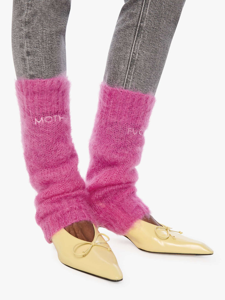 Side view of a woman in a legwarmer designed in a hot pink mohair blend with ribbed hems and MOTHER FUCKER in white across the front.