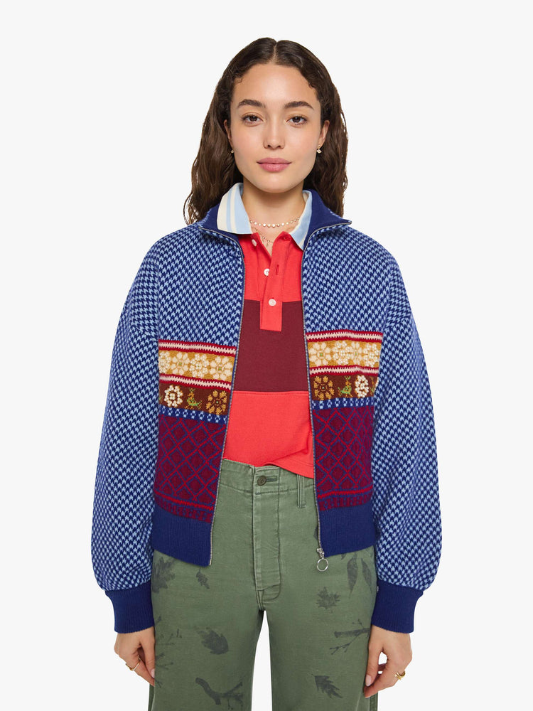 Front view of a woman in a navy and light blue Fleur de Lys pattern with colorful knit sections in red, golden yellow and maroon across the body and pearl beaded details sweater.