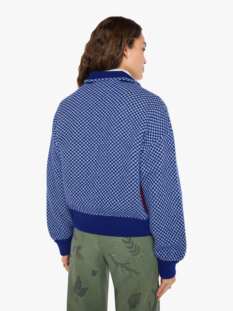 Back view of a woman in a navy and light blue Fleur de Lys pattern with colorful knit sections in red, golden yellow and maroon across the body and pearl beaded details sweater.