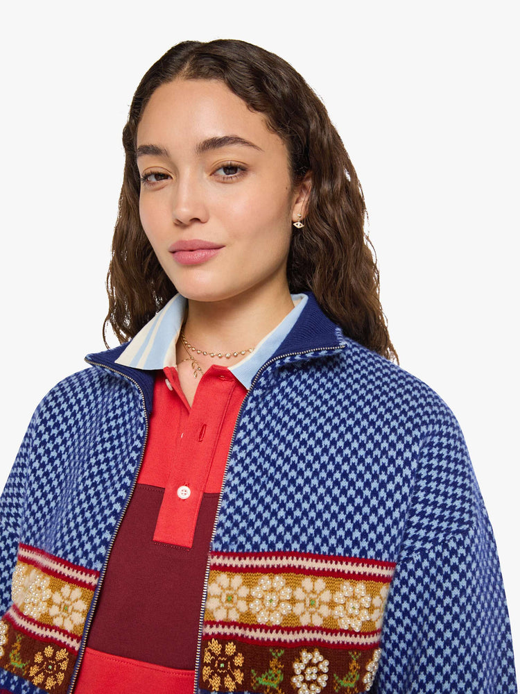 Close up view of a woman in a navy and light blue Fleur de Lys pattern with colorful knit sections in red, golden yellow and maroon across the body and pearl beaded details sweater.