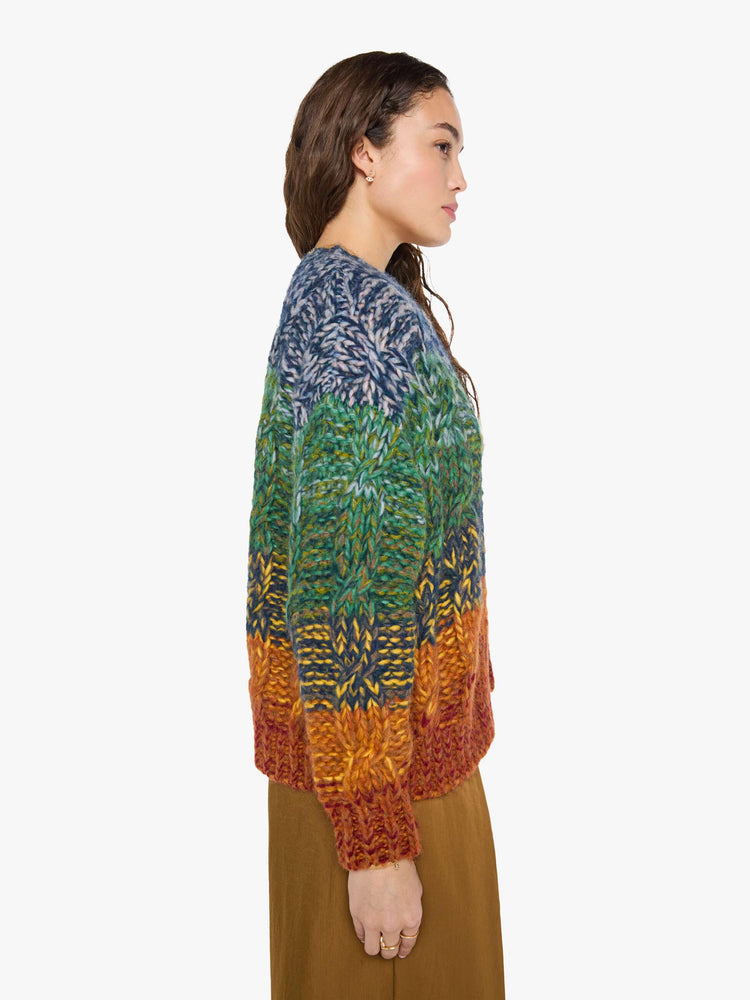 Side view of a woman in a rainbow stripe oversized cardigan with a crewneck, drop shoulders, ribbed hems and buttons down the front.