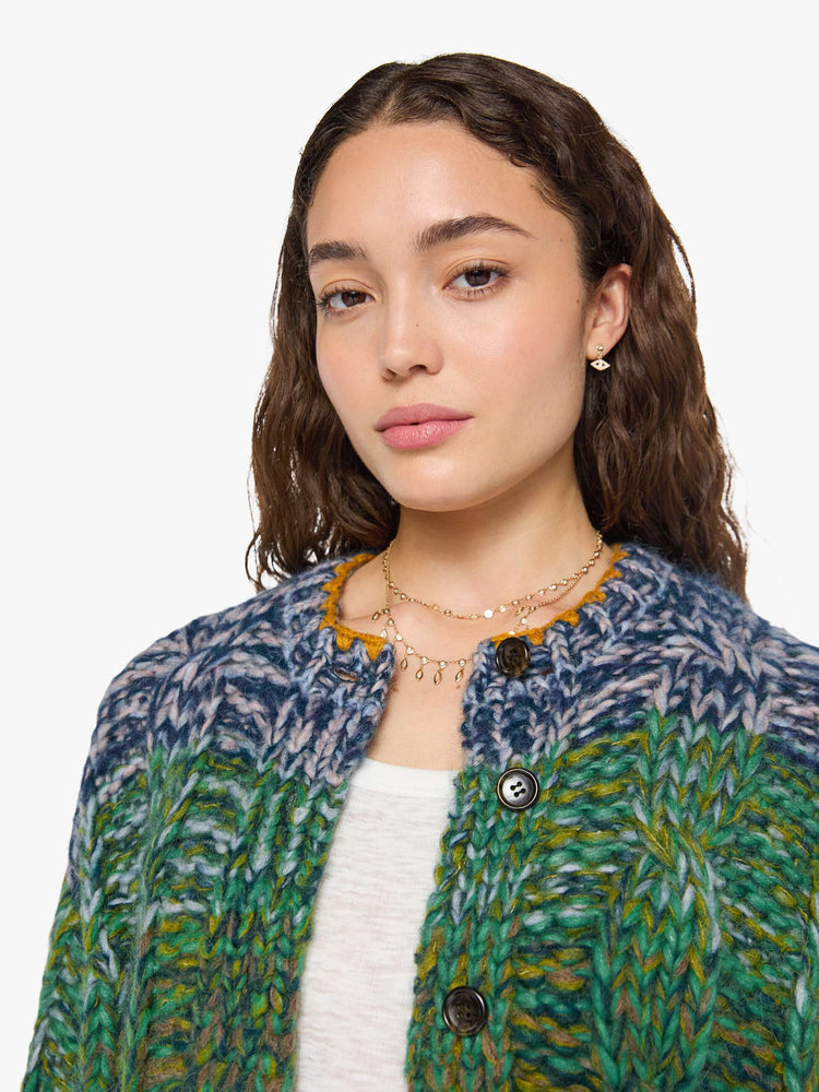 Close up view of a woman in a rainbow stripe oversized cardigan with a crewneck, drop shoulders, ribbed hems and buttons down the front.
