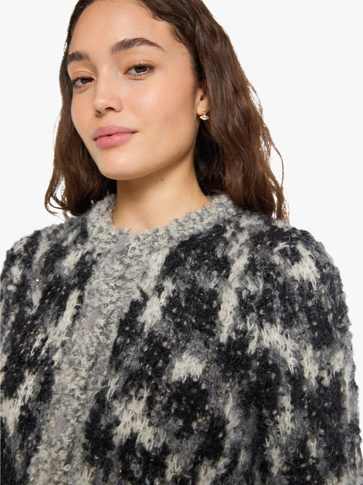Close up view of a woman in a sweater in a black, grey and white with beaded details throughout and faux-suede buttons down the front.
