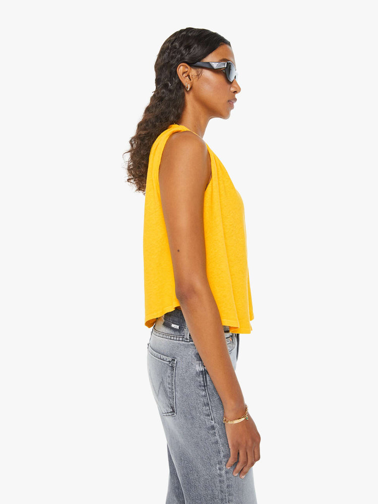 Side view of a woman in a yellow crewneck tank with gathered shoulders, a curved hem and a loose, oversized fit. Paired with grey jeans. 