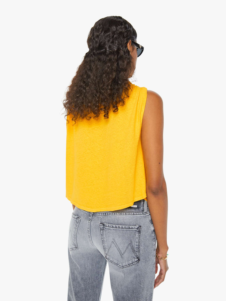 Back view of a woman in a yellow crewneck tank with gathered shoulders, a curved hem and a loose, oversized fit. Paired with grey jeans. 
