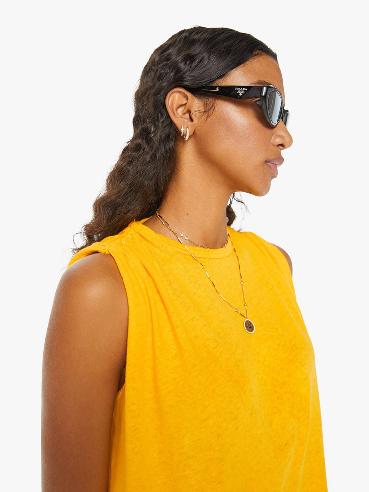 Detailed view of a woman in a yellow crewneck tank with gathered shoulders, a curved hem and a loose, oversized fit. 