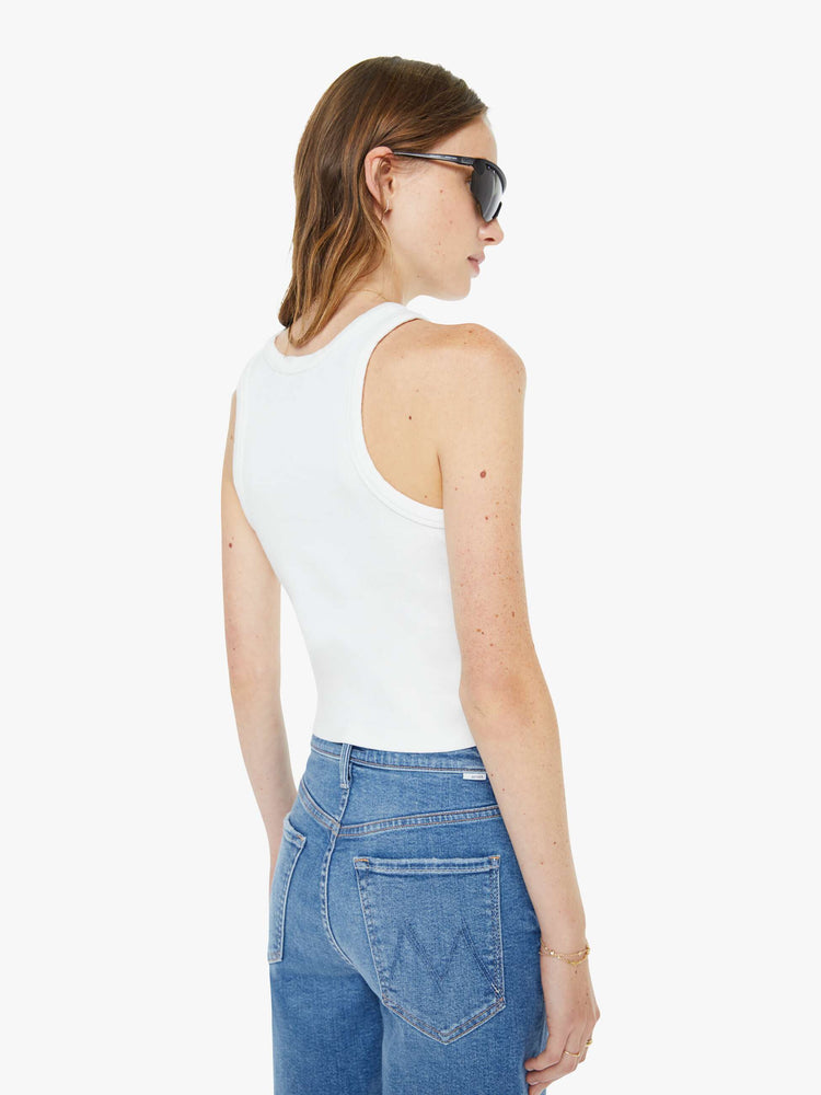 Back view of a woman in a white tank top with a airbrushed stencil text graphic in light blue on the front.