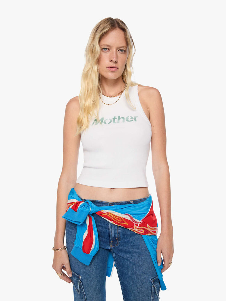 Front view of a woman in a cropped tank white with an airbrushed stencil text graphic of MOTHER's name in green on the front.
