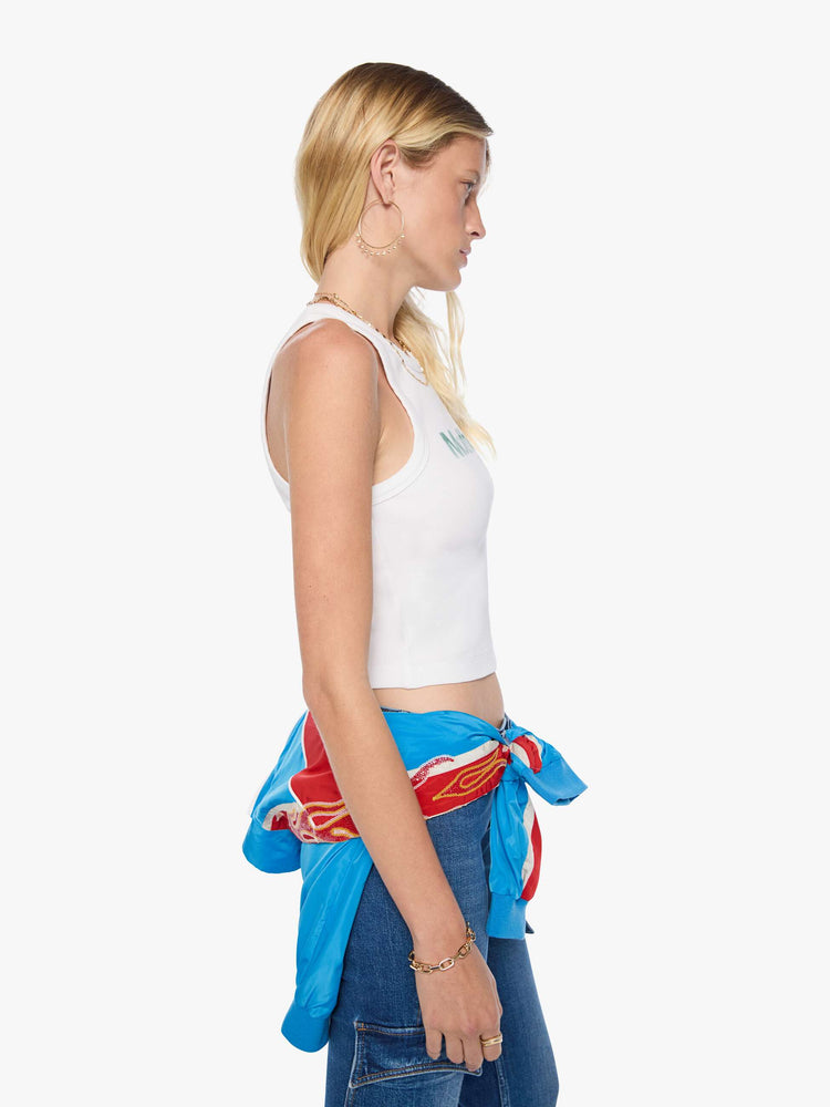 Side view of a woman in a cropped tank white with an airbrushed stencil text graphic of MOTHER's name in green on the front.