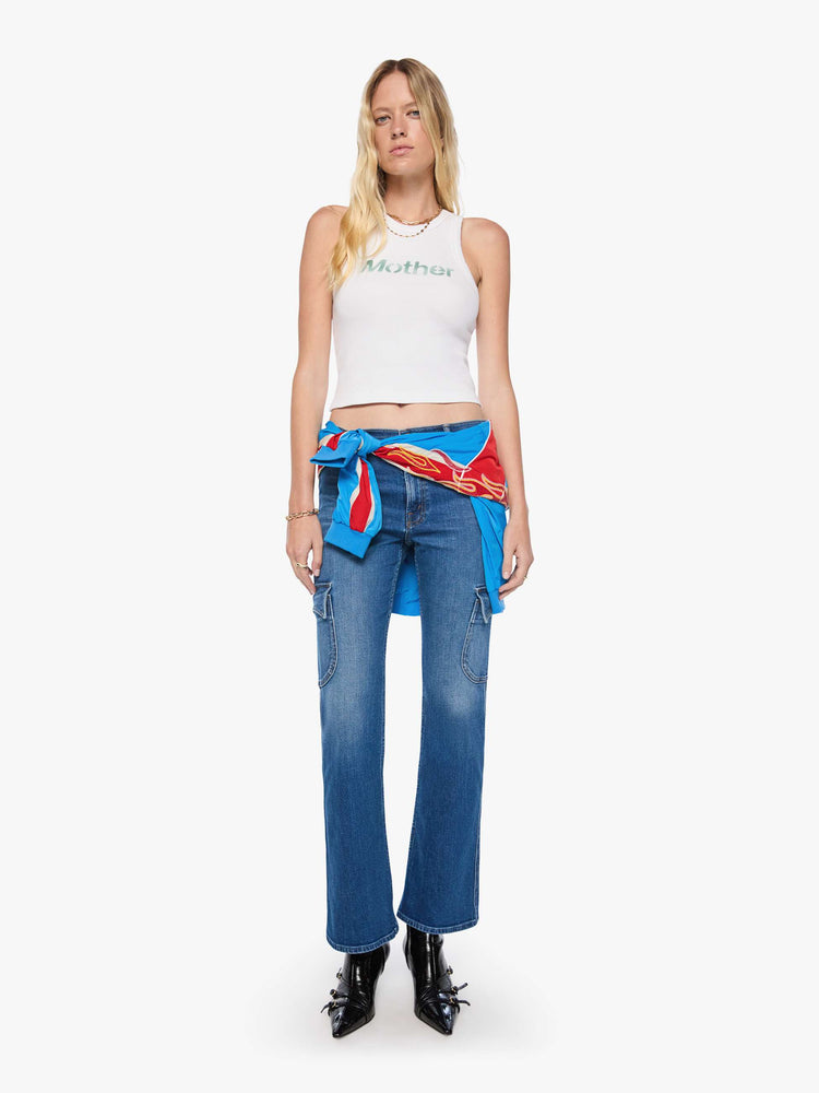 Full body view of a woman in a cropped tank white with an airbrushed stencil text graphic of MOTHER's name in green on the front.