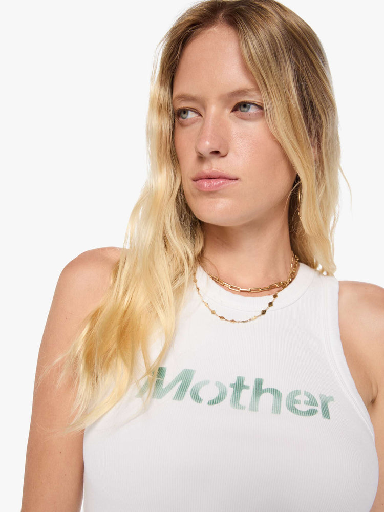 Close up view of a woman in a cropped tank white with an airbrushed stencil text graphic of MOTHER's name in green on the front.