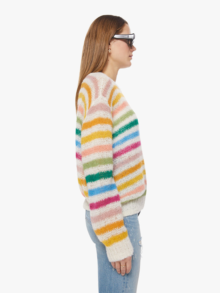 Side view of a woman oversized crewneck sweater with drop shoulders, long roomy sleeves and a hip-length hem in cream with horizontal rainbow stripes.