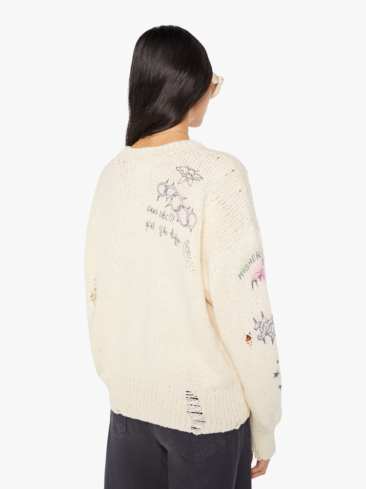 Back view of a woman in a cream  with faded hand-drawn doodles oversized crewneck sweater with drop shoulders and ribbed hems.