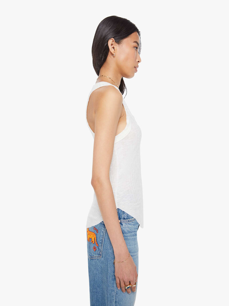 Side view of a woman in a white scoop neck tank with wide straps, a narrow fit and a curved hem. 