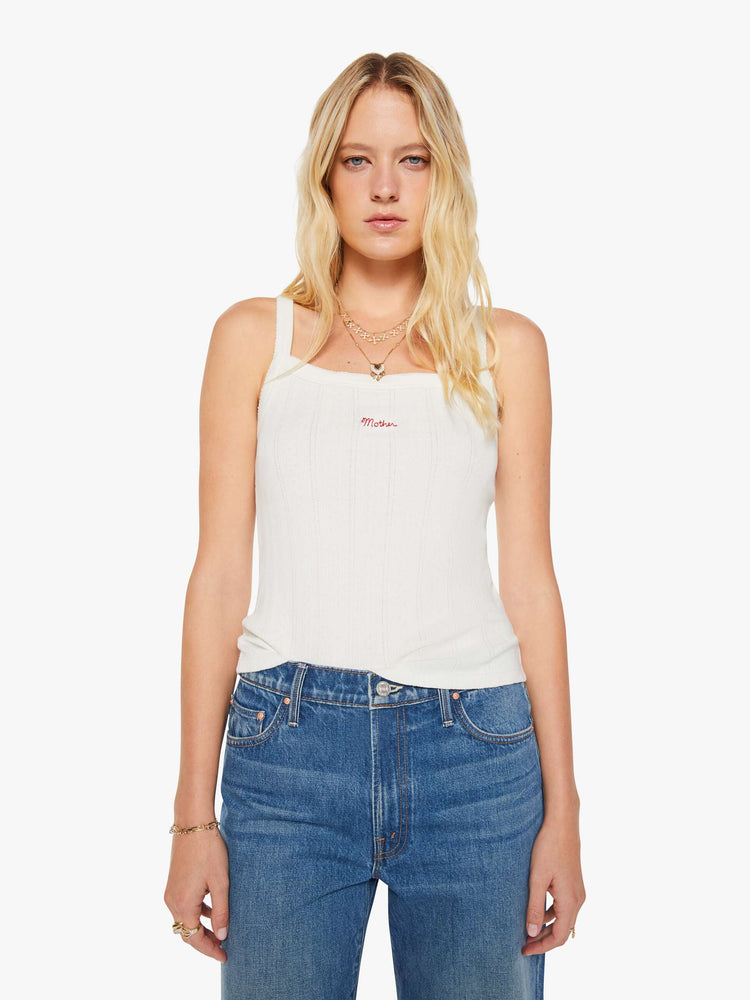 Front view of a woman in a square-neck tank with thick straps and a narrow fit. Made from 100% cotton, the top is designed in white with pointelle details and MOTHER's name embroidered in red on the front.
