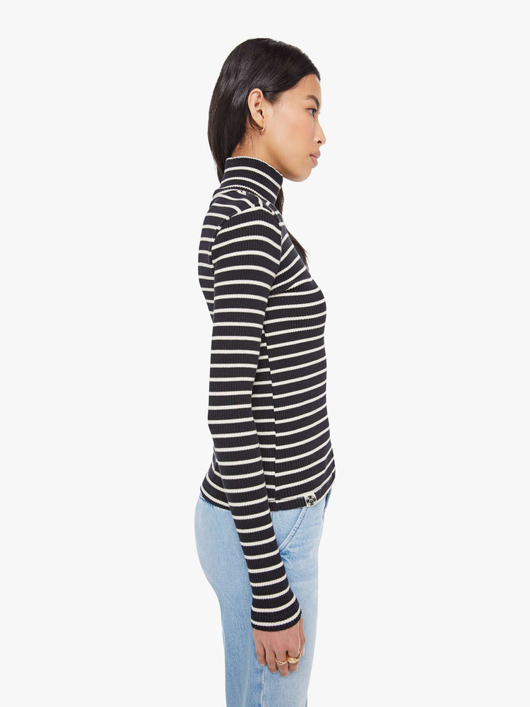 Side view of a woman in a black and white stripe long sleeve top with a folded turtleneck and a narrow fit.