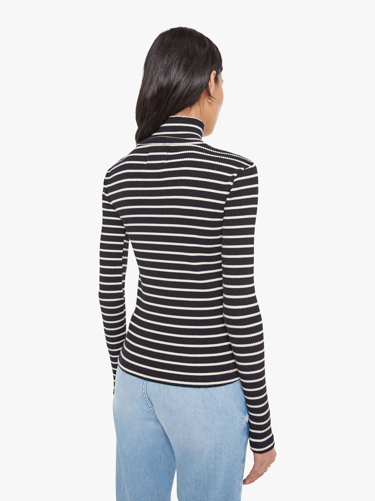 Back view of a woman in a black and white stripe long sleeve top with a folded turtleneck and a narrow fit.