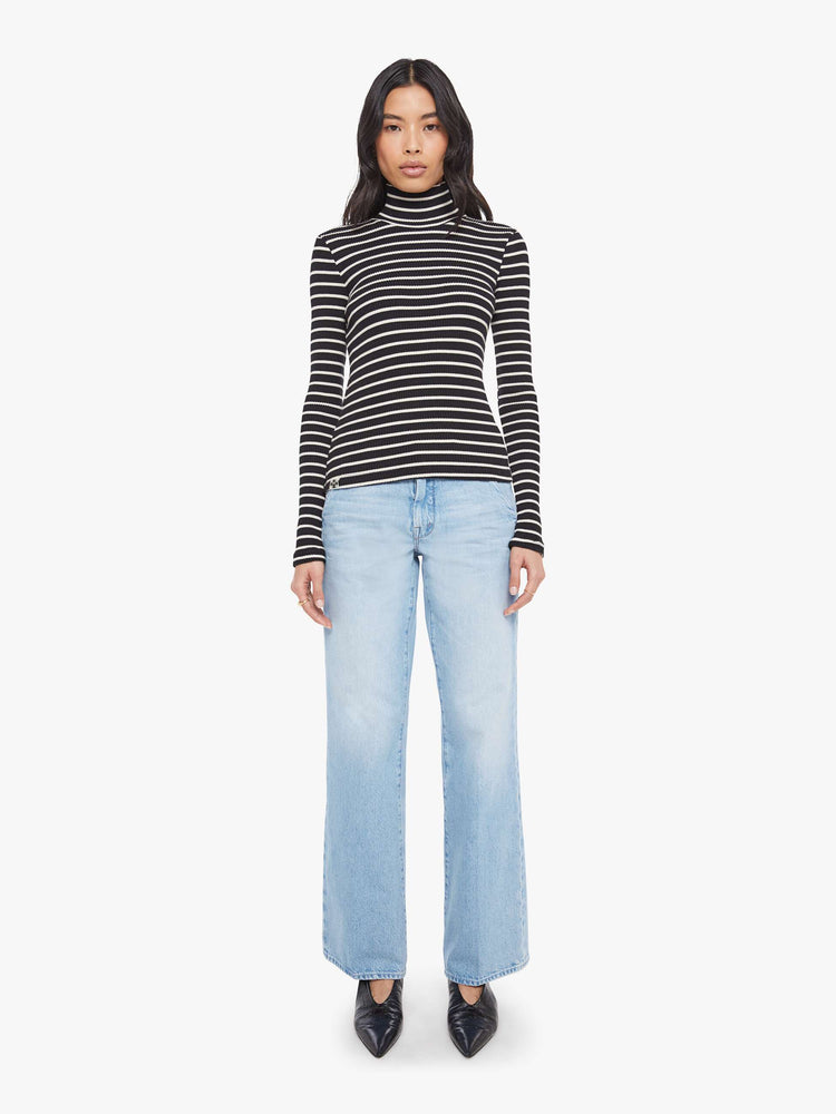 Full body view of a woman in a black and white stripe long sleeve top with a folded turtleneck and a narrow fit.