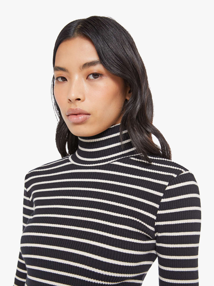 Close up view of a woman in a black and white stripe long sleeve top with a folded turtleneck and a narrow fit.