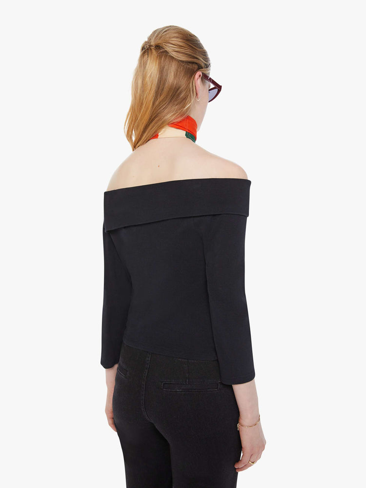 Back view of a woman in a black off-the-shoulder top with a folded neckline, 3/4-length sleeves and a narrow fit.