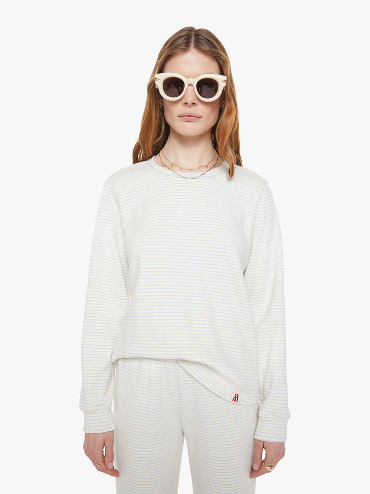 Front view of a woman in off-white with light blue horizontal stripes and a red M patch on the hem long sleeve tee.